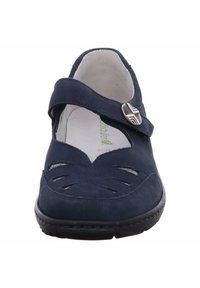 Marineblauwe suède schoen met een ronde neus, verstelbare band, uitsparingsontwerp op de vamp en zilverkleurige hardwaredetails. Platte rubberen zool.