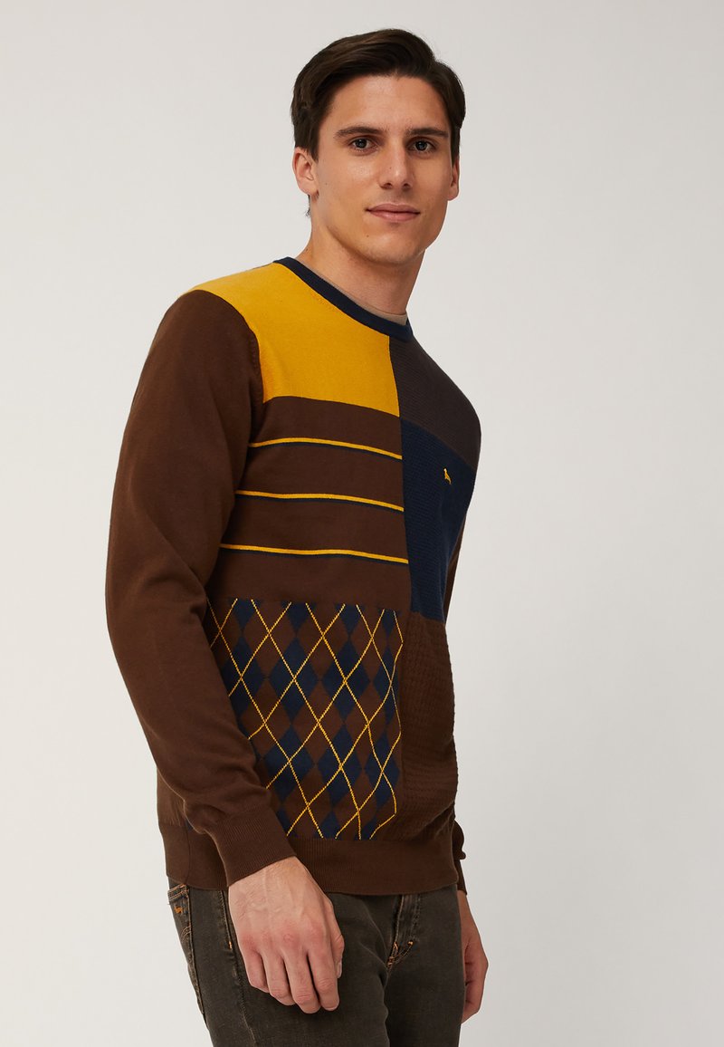Maglione color block con design diagonale marrone, giallo, blu navy e a fantasia. Texture lavorata a maglia con scollo a girocollo e polsini a costine.