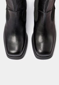 Czarne skórzane botki za kostkę o gładkim wykończeniu, kwadratowym nosku, elastycznych bocznych panelach i płaskiej gumowej podeszwie. Teksturowane powierzchnie i elegancki design.