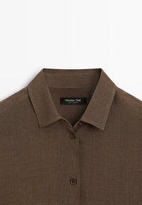 Chemise en lin marron à manches longues avec col pointu et deux boutons visibles, étiquetée Massimo Dutti.