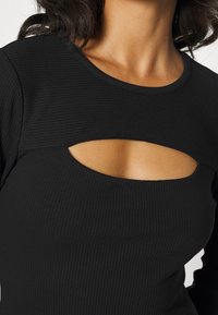 Haut noir à manches longues côtelé, doté d'un col dégagé avec un détail découpé, mettant en valeur une texture lisse et une coupe ajustée.