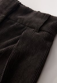 Gros plan sur un pantalon en tissu côtelé noir avec une taille haute et un motif vertical texturé en velours côtelé.