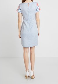 Light blue dress with short striped floral sleeves, featuring a central back zipper and fitted silhouette, paired with white high heels.