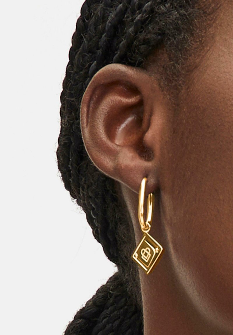 Goldene Ohrhänger mit einem diamantenförmigen Anhänger, der ein Logo trägt und vom Ring abgehängt ist, wobei eine glatte, polierte Oberfläche hervorgehoben wird.