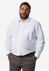 Camisa blanca de manga larga con cuello, cierre de botones en la parte delantera y un bolsillo en el pecho, combinada con pantalones oscuros de color marrón. Textura de tela suave.