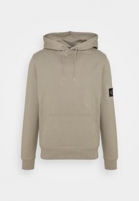 Beige mikina s kapucí, přední kapsou, stahovací šňůrkou a vroubkovanými manžetami. Na levém rukávu má černou nášivku s logem. Vyrobena z měkkého směsového bavlněného materiálu.