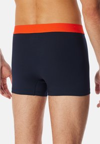 Boxer aderenti blu navy con un elastico arancione in vita. Presentano una texture liscia e un design aderente che si estende fino a metà coscia.
