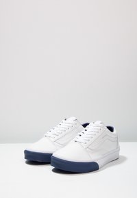 Sneaker in tela bianca con design a bassa punta, suola in gomma blu scuro e chiusura con lacci; presenta dettagli cuciti e una texture liscia.
