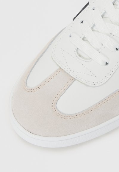 Pantofi sport albi și bej din materiale din suede și piele, cu vârf rotund, șireturi plate și detalii subtile de coasere.