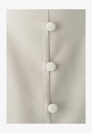 Gai beidža audums ar gludu tekstūru, kura centrā ir trīs baltas, apaļas pogas, padarot dizainu simetriskiem.