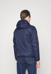 Giacca puffer blu navy con cappuccio, caratterizzata da una texture liscia, un design aderente e polsini elasticizzati. Stile semplice e funzionale.