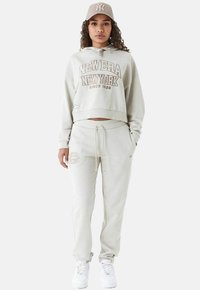 Felpa corta grigia chiara con la scritta "New Era New York", pantaloni abbinati e un cappello beige. Realizzata in tessuto morbido e con una vestibilità rilassata.