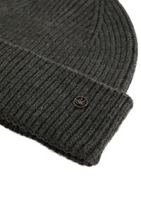 Tumši pelēks adīts cepure ar ribotu tekstūru, kas satur nelielu metāla logotipa akcentu sānos. Mīksts vilnas materiāls.