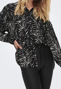 Zebra print shirt in zwart-wit met een knoopsluiting aan de voorkant, lange mouwen en een losse pasvorm, gecombineerd met high-waisted zwarte broek.