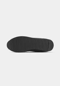 Black rubber shoe sole with a ridged texture and rounded toe. Features a visible logo and a flat profile for stability.