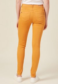 Yellow skinny jeans feature a fitted design, five pockets, and a smooth texture, styled with a mid-rise waist and subtle stitching details.