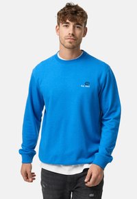 Sudadera de algodón azul con mangas largas, cuello y dobladillo acanalados. Presenta un logotipo blanco y bordado "Est. 1993" en el pecho.