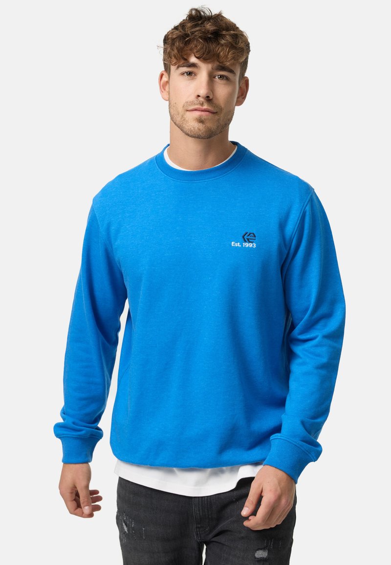 Sudadera de algodón azul con mangas largas, cuello y dobladillo acanalados. Presenta un logotipo blanco y bordado "Est. 1993" en el pecho.