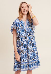 Blaues und weißes gemustertes Kleid mit kurzen, fließenden Ärmeln, V-Ausschnitt und einem fransigen Saum. Verziert mit floralen Motiven und dekorativer Borte.