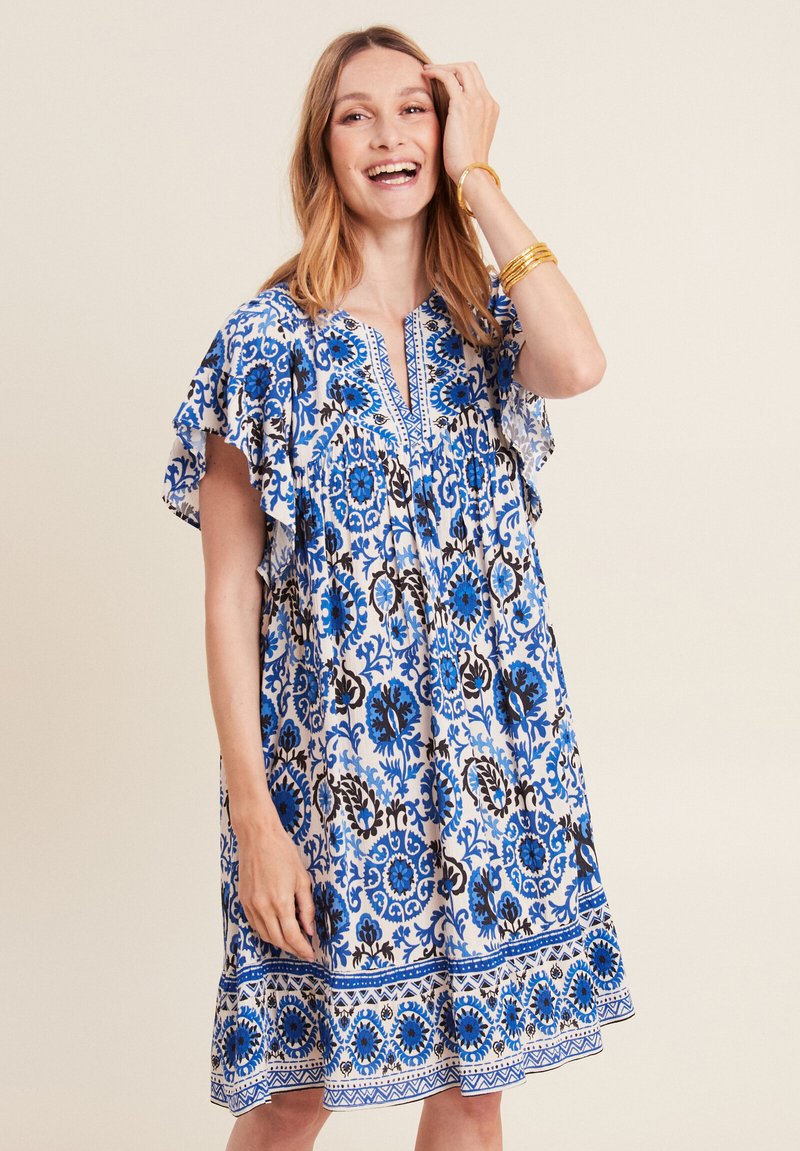 Blaues und weißes gemustertes Kleid mit kurzen, fließenden Ärmeln, V-Ausschnitt und einem fransigen Saum. Verziert mit floralen Motiven und dekorativer Borte.