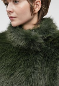 Zielona sztuczna futrzana odzież z wysokim kołnierzem, charakteryzująca się miękką, teksturowaną powierzchnią i różnymi odcieniami zieleni, zaprezentowana w zbliżeniu.