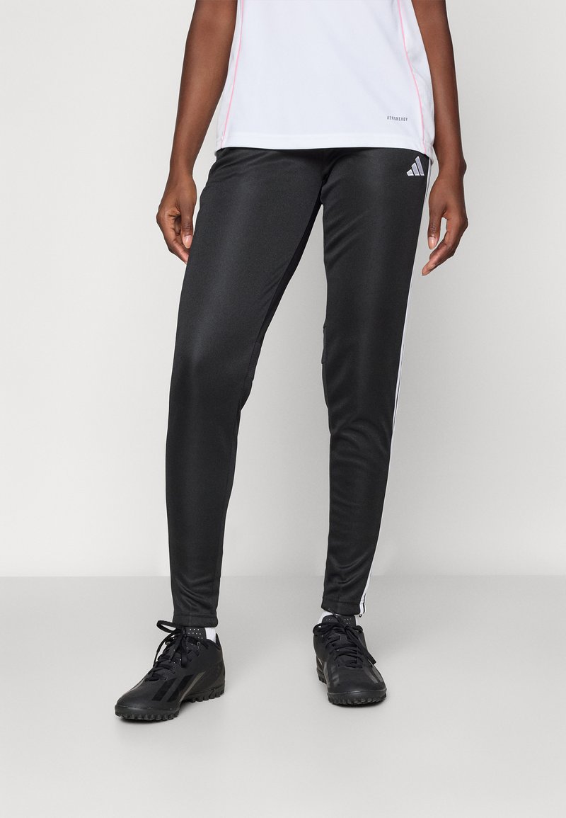 Black athletic pants with a smooth texture, featuring white side stripes, paired with black sports shoes. The shirt is white with pink accents.