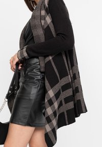 Cardigan a fantasia nera e beige con apertura anteriore, texture lavorata a maglia, maniche lunghe, design drappeggiato, abbinato a una gonna in pelle nera.