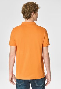 Polo shirt in cotone arancione con maniche corte, colletto e design semplice. Presenta un accento verde sulla manica. Vista posteriore semplice.