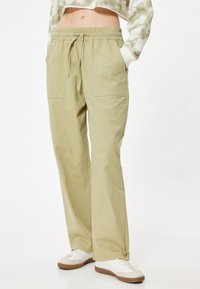 Helle olivgrüne Hose mit elastischem Bund, verstellbarem Kordelzug und zwei Fronttaschen. Glatte, gewebte Stofftextur.