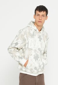 Felpa bianca con un motivo a foglia grigia, dotata di tasca frontale, cappuccio con cordino e logo "GAP" in bianco. Polsini e orlo elasticizzati.