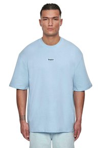 Lyseblåt bomulds oversized t-shirt med korte ærmer, rund halsudskæring og et lille sort mærke med ordet "Dropsize" på brystet.