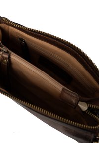 Interno di una borsa in pelle marrone con dettagli cuciti, dotata di chiusura con zip, due tasche e una fodera beige liscia.