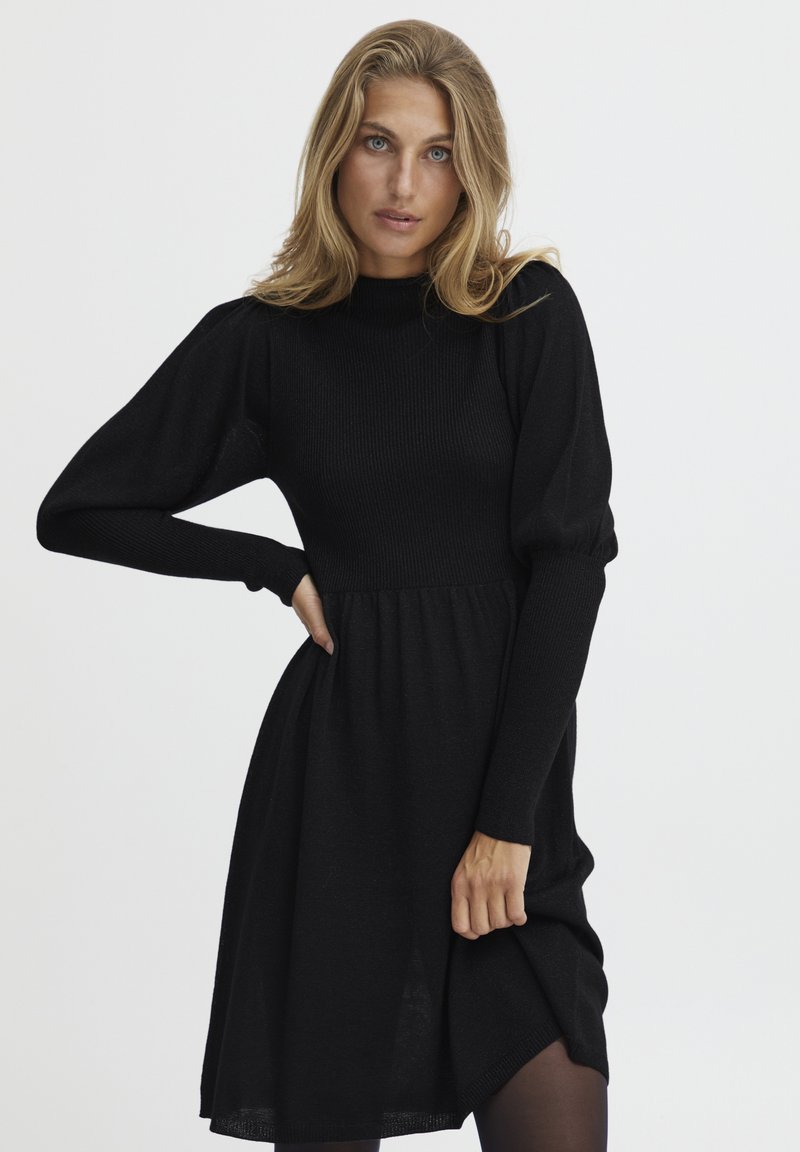 Rochie tricotată neagră cu guler înalt, mâneci lungi bufante și bust ajustat, trecând la o fustă evazată. Textură netedă.