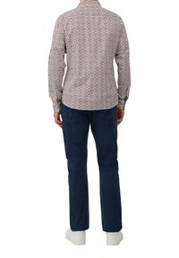 Langarmshirt met een multikleurig geometrisch patroon op een witte achtergrond, gecombineerd met donkerblauwe broek en witte sneakers.