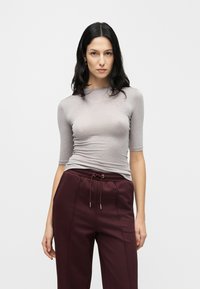 Chemise grise cintrée à manches mi-longues, réalisée dans un tissu lisse. Associée à un pantalon jogger bordeaux avec une taille à cordon de serrage.