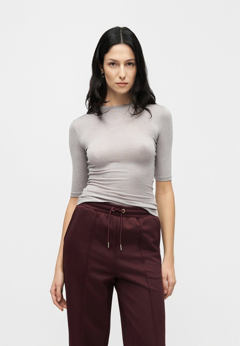 Chemise grise cintrée à manches mi-longues, réalisée dans un tissu lisse. Associée à un pantalon jogger bordeaux avec une taille à cordon de serrage.