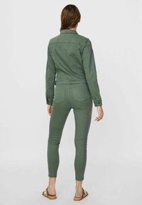 Grön denimjacka med en figursydd silhuett, kombinerad med matchande figursydda byxor. Båda plaggen har minimal sömnad och fickor.