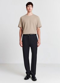 T-shirt beige a maniche corte abbinato a pantaloni neri eleganti, con una texture liscia e un design semplice, completato da scarpe nere.