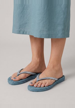 Pies con chanclas azules texturizadas con tiras plateadas, combinados con una falda o vestido azul claro hasta la rodilla.