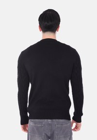 Maglione nero con motivo a trecce sulle maniche, polsini e orlo a coste. Realizzato in un tessuto morbido, presenta un collo rotondo.