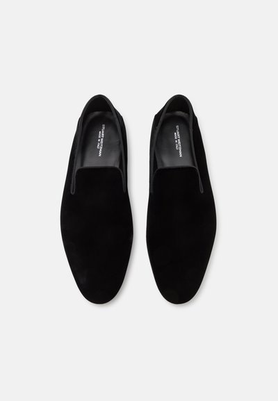 Black suede slip-on shoes with a smooth texture, rounded toe, and minimal stitching. Labeled interior with brand name.