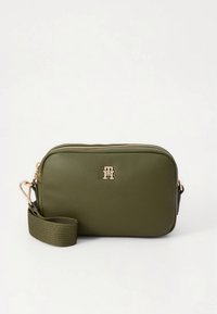 Olijfgroene crossbodytas van synthetisch leer met een gouden logo, ritssluiting en een gevlochten band. Rechthoekige vorm met een gladde textuur.