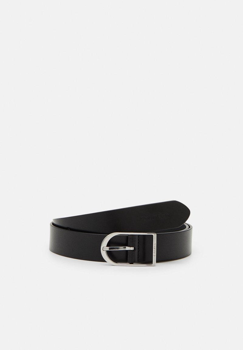 Ceinture en cuir noir avec une boucle métallique argentée en forme de D, partiellement enroulée sur un fond blanc uni.
