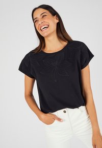 Zwarte katoenen t-shirt met tonale bloemembroidery op de voorkant, korte mouwen en een losse pasvorm, gecombineerd met witte jeans.