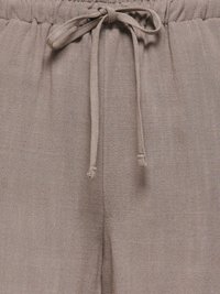 Pantalon en tissu taupe avec ceinture élastique et cordon noué, montrant un motif texturé subtil sur le matériau.
