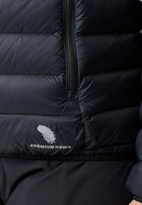 Sort pufferjakke med quiltet design, der har en lynlås foran og "PREMIUM DOWN"-logo i hvidt ved kanten. Blød tekstur.
