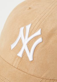 Căciulă de baseball bej, realizată dintr-un material moale, având un logo alb brodat al echipei New York Yankees. Detalii cusute pe panta și vizor.
