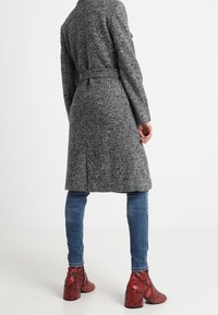 Cappotto grigio in lana con texture e cintura, abbinato a jeans skinny blu e stivali alla caviglia in stampa rettile rossa.