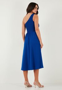Blue, one-shoulder dress with a smocked bodice, flowing skirt, and ankle-length design; lightweight fabric with a textured finish.