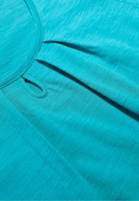 Tyrkysový látkový top s kulatým výstřihem, detailním skladem a měkkým, texturovaným povrchem. Ploché švy a jemné melírování přidávají hloubku.